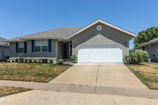 Front view of a single-story suburban house with a two-car garage, driveway, and neatly landscaped yard, representing a typical home used in real estate note investing.